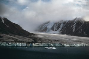 Discover the breathtaking beauty of Arctic with top tours showcasing a vast, icy landscape. Snow-capped mountains and glaciers meet a dark blue sea, where icebergs gently float under a cloudy sky, crafting a dramatic yet serene scene.