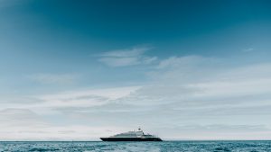 A luxurious yacht sails on the vast ocean under a wide, cloudy sky with a gradient of blues. The distant horizon stretches across the scene, evoking the serenity one might seek when pondering how to visit Antarctica and embark on such an extraordinary journey.