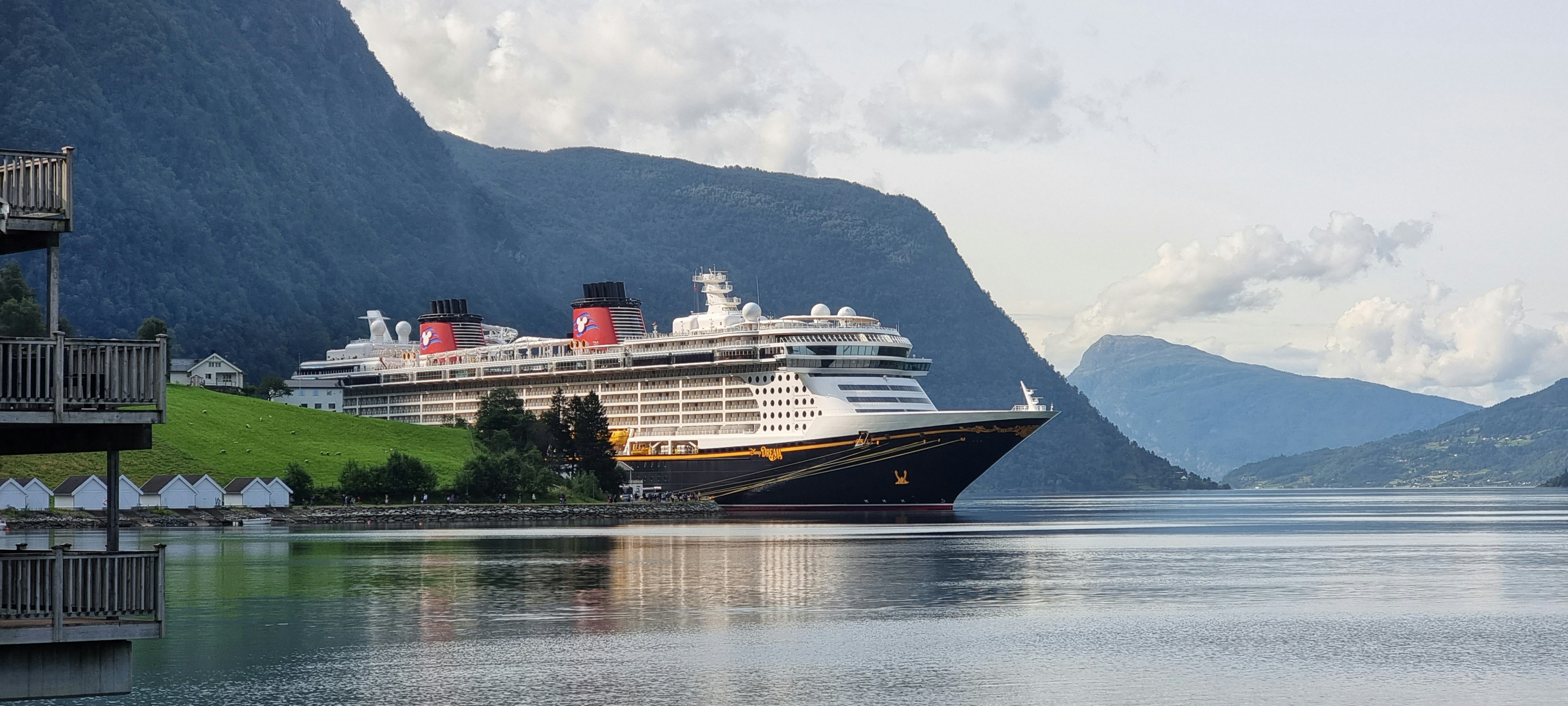 A large cruise ship docked at a small village surrounded by green hills and mountains, with calm water reflecting the scenery—an idyllic scene reminiscent of the Best Trips to Antarctica for 2026, where adventure meets breathtaking beauty.
