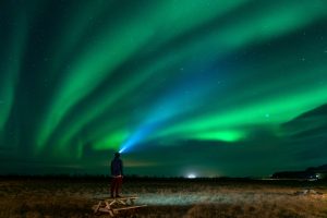 Man with headlamp obesrving green and blue northern lights in Iceland