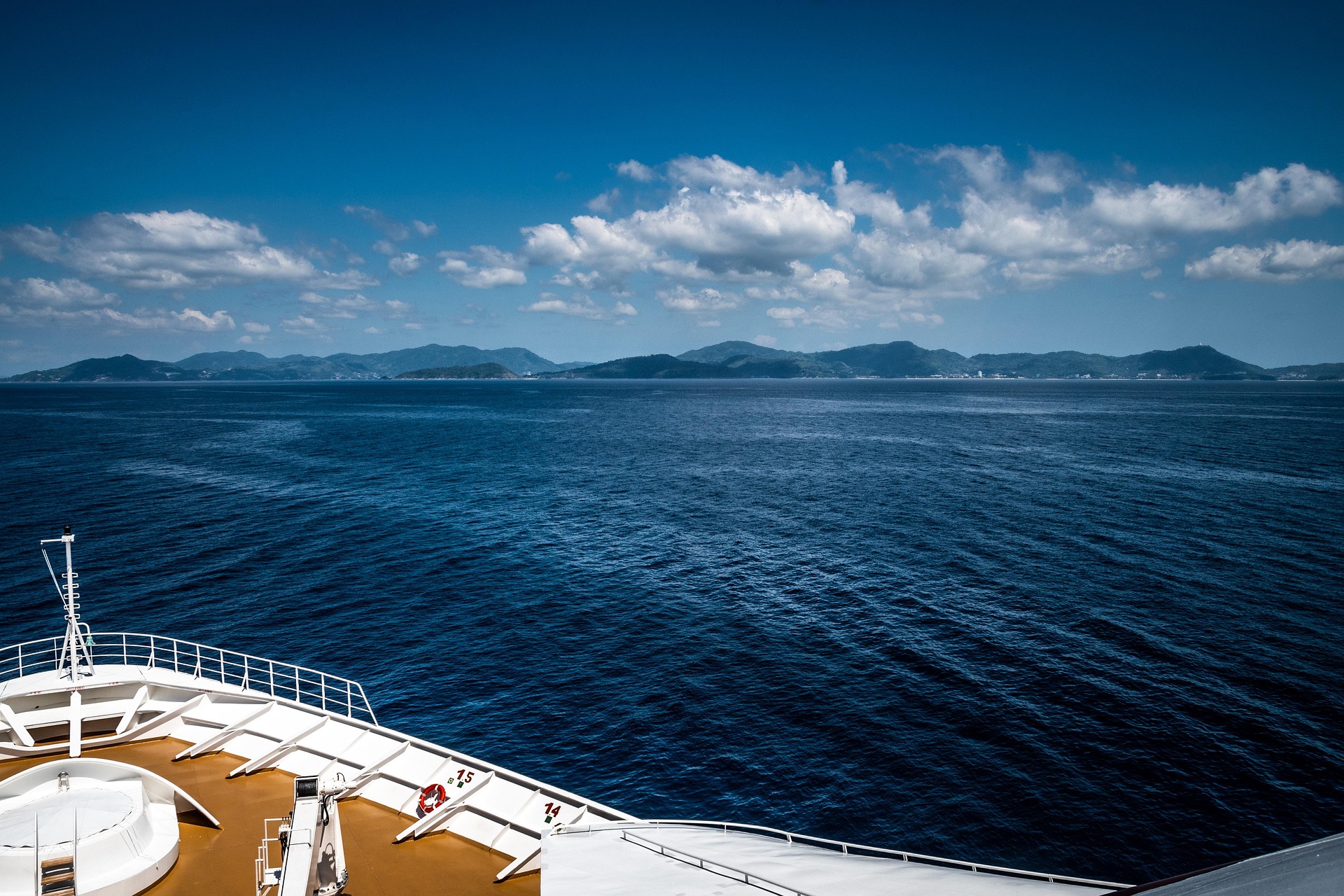 View from the bow of a cruise ship sailing on deep blue water under a partly cloudy sky, with distant green mountains—an unforgettable scene for those seeking Antarctica honeymoon trips.